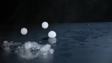 İçinde duman olan sabun köpükleri siyah bir masaya düşer ve patlar. Yavaş Hareket Koyu Arkaplan.