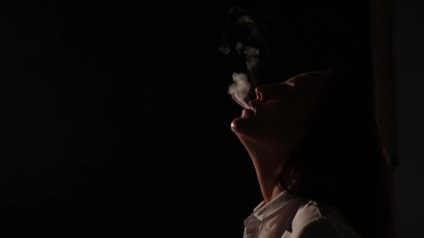 Pensive brunette in een wit shirt rookt een hookah in het donker. Portret van een vrouw die een vape rookt, zwevend. Zwarte achtergrond. Elektronische sigaret. Slechte gewoonte. — Stockvideo