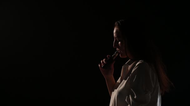 흰 셔어 츠 를 쓴 음흉 한 브루 네트 는 어두운 곳에 있는 후카 를 질식시킨다. 증기를 피우고 떠 있는 여자의 사진. 검은 배경. 전자 담배. 나쁜 습관. — 비디오