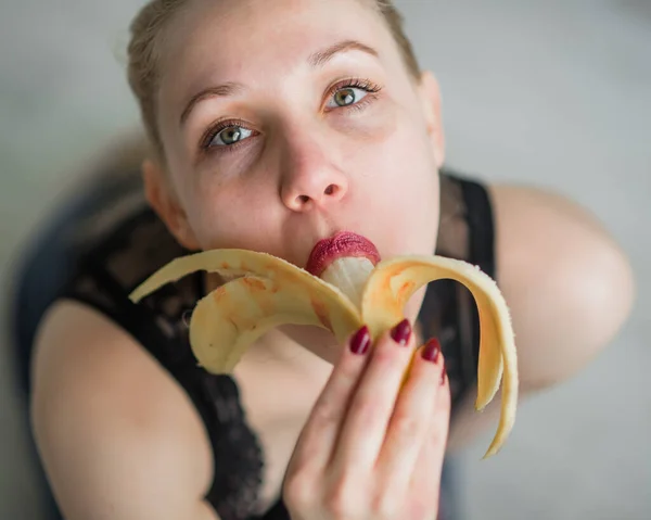 The concept of oral sex. Girl with blond hair, sexy licks and caresses lips and tongue big banana on the bed in the bedroom. Erotic fantasy. Seduction. View from above. — Stockfoto