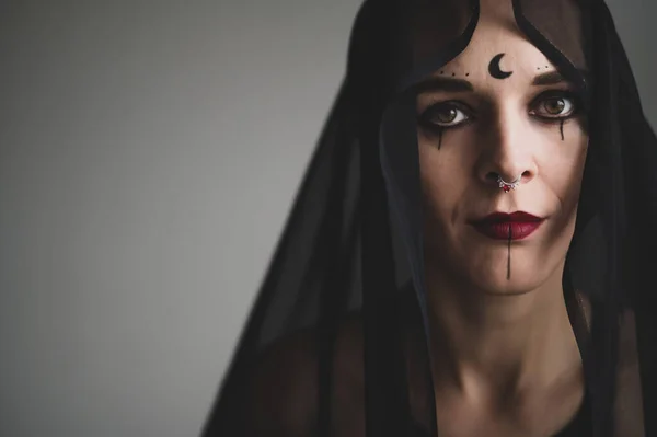 A grinning woman in a black veil with dark makeup and an earring in her nose. Halloween Dead Bride Costume. Portrait of the sinister Witch in front of the coven.
