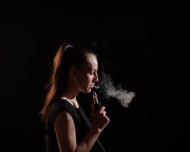 Esmer, siyah arka planda elektronik bir sigara içiyor ve ağzından yoğun bir duman salıyor. Bir kadın portresi sigara içiyor, havada süzülüyor..