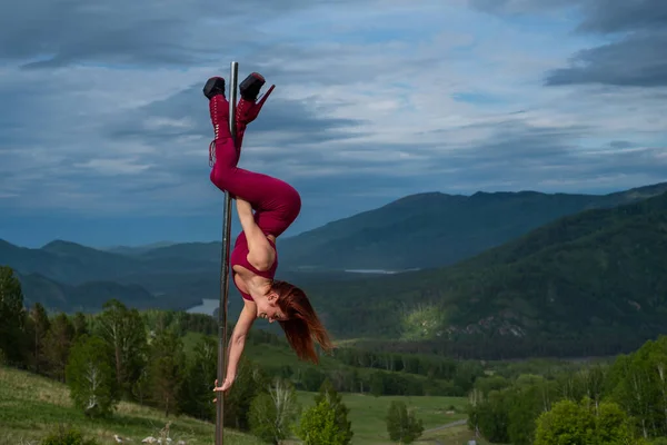 Güzel kızıl saçlı kadın dağların arka planında taşınabilir bir platformda dans ediyor. Kız direğin yanına cinsel olarak taşınıyor. Dersler için tulum. Yüksek topuklu. Altai. Müthiş esneklik. — Stok fotoğraf