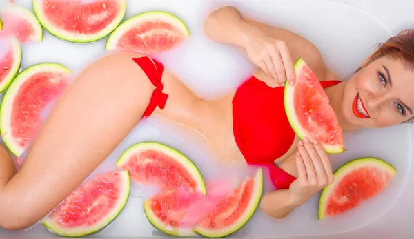 A slender woman takes a milk bath with slices of watermelons. SPA skin care  treatments. Girl in a red bikini. Red lipstick. Likes in the jacuzzi.  Cleopatra Rejuvenation. View from above. Beautiful