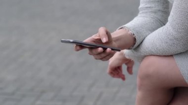 Düzgün manikürlü bir kadın parmağını telefonun ekranından geçirir. Mola sırasında takım elbiseli bir kız dışarıda akıllı telefonuyla mesajlaşıyor..