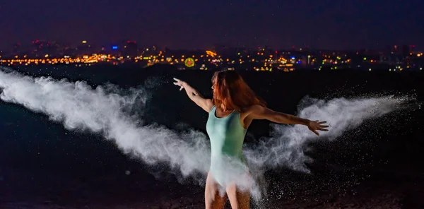 Mulher de cabelos vermelhos em um bodysuit azul dançando em nuvens de farinha. Uma menina na margem do rio saltando espalhando pó branco . — Fotografia de Stock