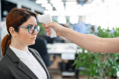 Ofis personeli için elektronik kızılötesi termometre ile sıcaklık ölçümü. Ateşi olan mutsuz bir kadın. Termometre tabancasıyla yapılan zorunlu kontrol, temassız bir alın okumasıdır. Coronavirüs