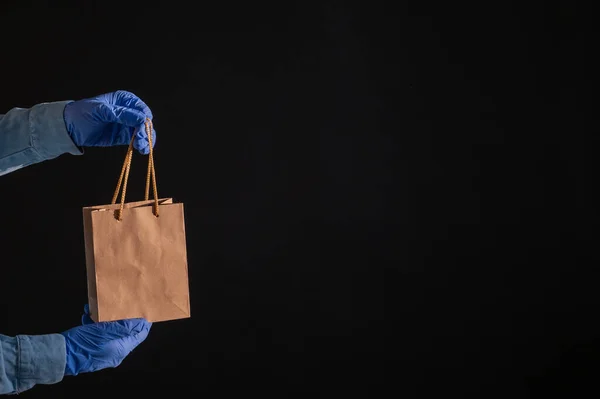 Entrega a domicilio expresa en la epidemia de coronavirus. Mensajero en guantes con una bolsa de papel. Embalaje hecho de material reciclado ecológico. Comprar productos en línea en cuarentena . — Foto de Stock