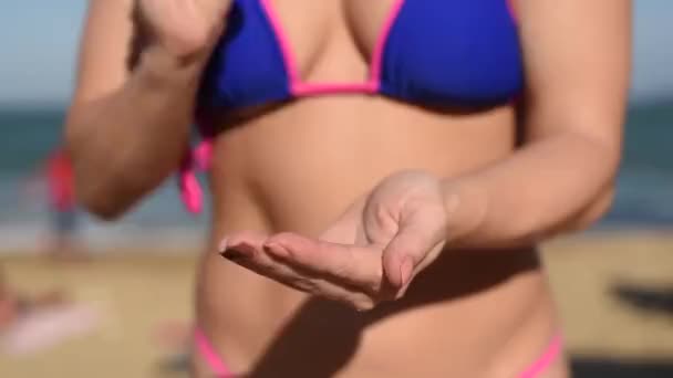 Close-up van een vrouw die zonnebrandcrème met een ondiepe scherptediepte aanbrengt. Meisje in bikini knijpt zonnebrandcrème op haar hand.Vrouw zonnebaden op de zee in sexy bikini. — Stockvideo