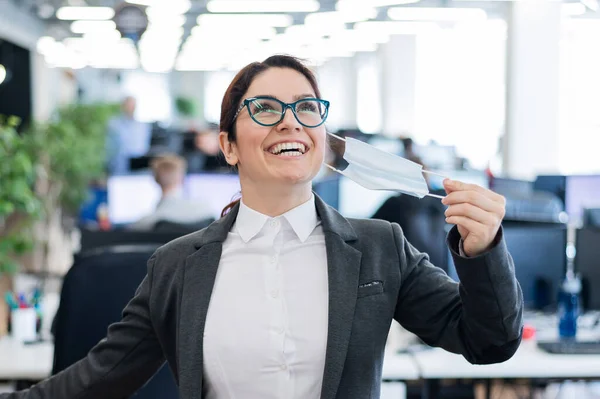 İş kadını, karantinanın sonunda ofisteki maskeyi çıkarır. Coronavirus zaman içinde işe geri dönecek. Kız özgürce nefes alıyor ve gülümsüyor. Salgına karşı zafer. Normale dön..