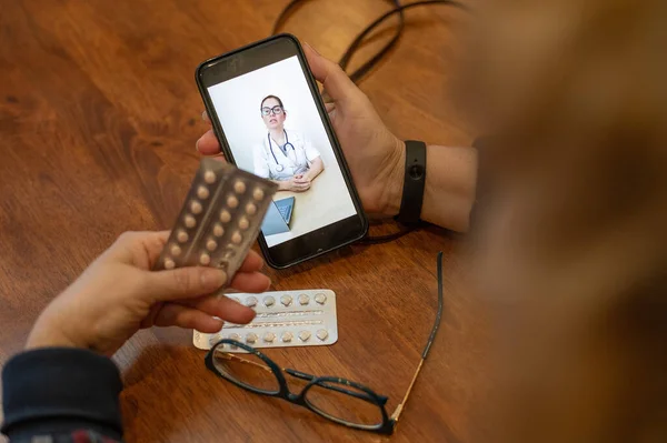 Online consultation. The doctor talks to the patient on a video call. An elderly woman has the flu. A quarantined pensioner communicates with her doctor by phone. Hands of an old woman.