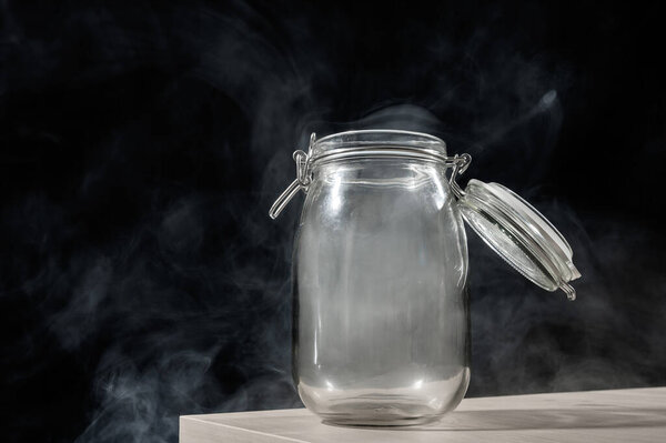 Стеклянная банка с крышкой, наполненной дымом на черном фоне. Туман в прозрачном контейнере на столе
.