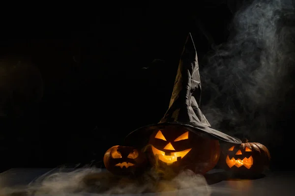 Τρομακτικές πορτοκαλί κολοκύθες για Halloween σταθεί στη σειρά σε ένα σκοτεινό φόντο. Ο Τζακ Ο Λάντερν με καπέλο μάγισσας. Η μυστικιστική ομίχλη σέρνεται στο έδαφος. Φάρσα ή κέρασμα. — Φωτογραφία Αρχείου