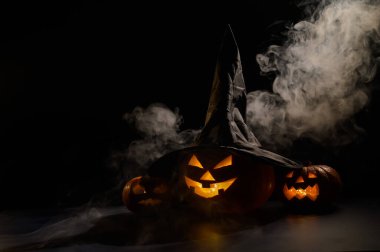 Cadılar Bayramı için ürkütücü turuncu balkabakları arka planda arka arkaya duruyor. Cadı şapkalı Jack O Lantern. Mistik sis yerde sürünüyordu. Şaka mı şeker mi?.