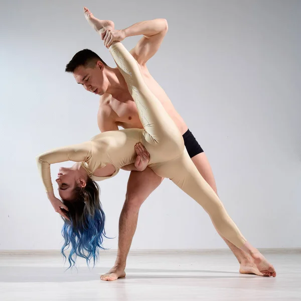 Une paire de danseurs en action. Un jeune duo d'artistes de cirque joue avec de la ficelle en studio. Homme en caleçon tenant Femme en salopette pour la gymnastique dans les fentes. — Photo