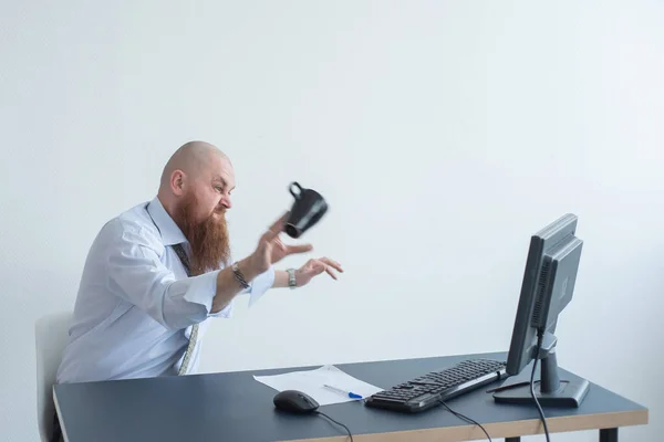 En skäggig man har ett nervöst sammanbrott på jobbet. Kontorschefen flippar ut och bryter en mugg på monitorn. — Stockfoto