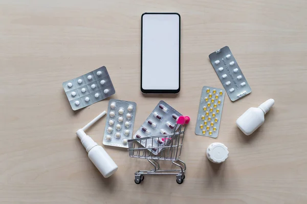 Farmacia en línea. Aplicación de Smartphone para comprar medicamentos. Vista superior de un mini carrito de la compra con blisters de tabletas y un teléfono . — Foto de Stock