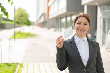 Takım elbiseli bir kadın öğle arasında sokakta yürür ve maskesini çıkarır. Karantinaya alınmış Coronavirus yenildi. Tecrit bittikten sonra işe dönüyorum..