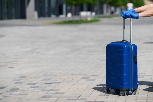 Primer plano de una mano femenina en un guante en un asa de equipaje. Una mujer está caminando por la calle y con una gran bolsa azul. Concepto de viaje durante un brote de virus. Higiene personal — Foto de Stock