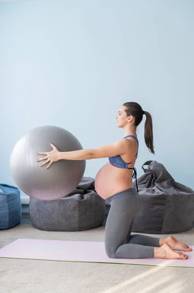 Zwangere Europese vrouw voert oefeningen met fitness bal. Verwachte moeder doet yoga in het derde trimester. Meisje in de klas ter voorbereiding op de bevalling. — Stockfoto