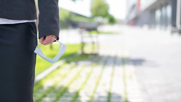 Närbild av kvinnliga händer med en medicinsk mask. Affärskvinnan tog av masken på gatan. Coronavirusepidemin är över. Slut på karantänen. — Stockfoto