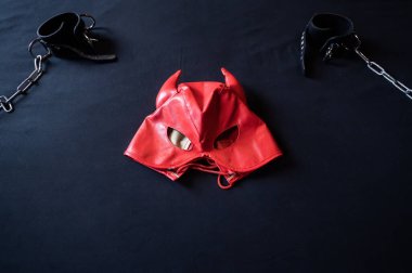 BDSM ekipmanları. Kırmızı deri bir şeytan maskesi ve gri bir çarşafta zincirli siyah kelepçeler. Seks oyuncakları. Hakimiyet. Kimse yok..