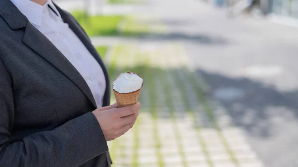 顔のないビジネスマンの女性は屋外を歩き、晴れた夏の日にバニラアイスを食べます。アイスクリームコーンと女性の手のクローズアップ. — ストック写真