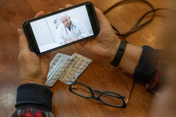 Інтернет-ліки. Стара жінка з коронавірусними симптомами розмовляє на смартфоні з вірусологом. Чоловік слухає скарги на здоров'я літньої жінки на відеозв'язку . — стокове фото