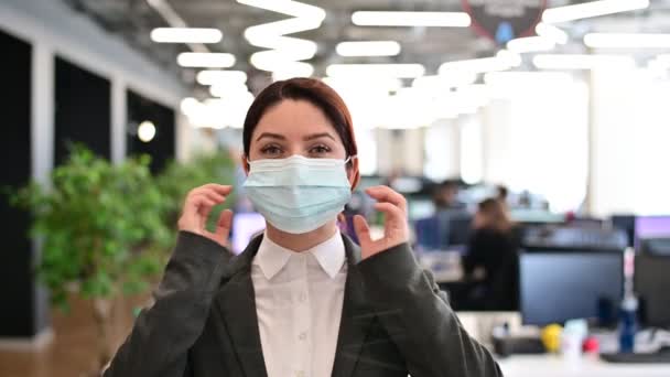 Fröhliche Frau im Anzug zieht im Büro eine medizinische Maske aus. Geschäftsfrau feiert Quarantäne-Ende Sieg über das Virus. Festliche Stimmung. Freie Ausatmung ohne Maske. — Stockvideo