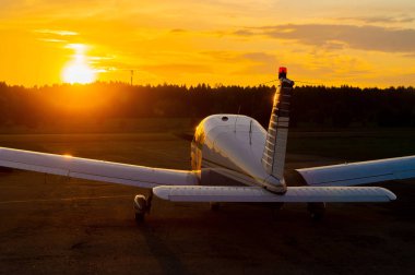 Gün batımı arka planında park etmiş küçük bir uçağın arka görüntüsü. Alacakaranlıkta yere çakılmış özel bir jetin silueti. Piper Cherokee bireysel pervane uçağı