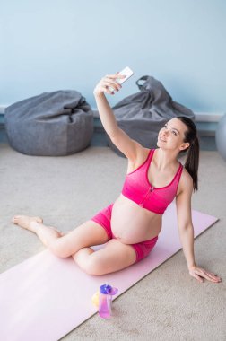 Hamile bir kadın yoga minderinde selfie çekiyor. Beyaz bir anne pilates yaparken akıllı bir telefonla fotoğraflanır..