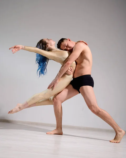 Acrobatic couple perform number on a white background. A duet of gymnasts rehearsing a performance with support. A man and a very flexible woman are dancing.