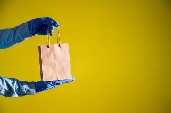 Female courier hand in medical latex gloves holds a small paper bag. Safe delivery during the spread of coronavirus. Ecofriendly packaging. Online shopping. — Stock Photo, Image