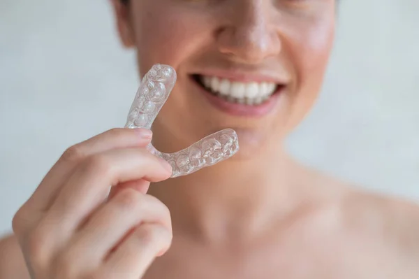 Close-up de dentes transparentes de silicone ortodôntico aligner em mãos femininas. Mulher irreconhecível segurando um retentor de noite removível. Suporte para clareamento dos dentes. O sorriso perfeito. Foto cortada. — Fotografia de Stock