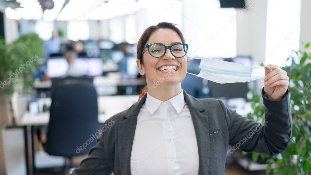 Business woman takes off the mask in the office at the end of quarantine. Coronavirus over time to return to work. The girl breathes freely and smiles. Victory over the pandemic. Return to normal.