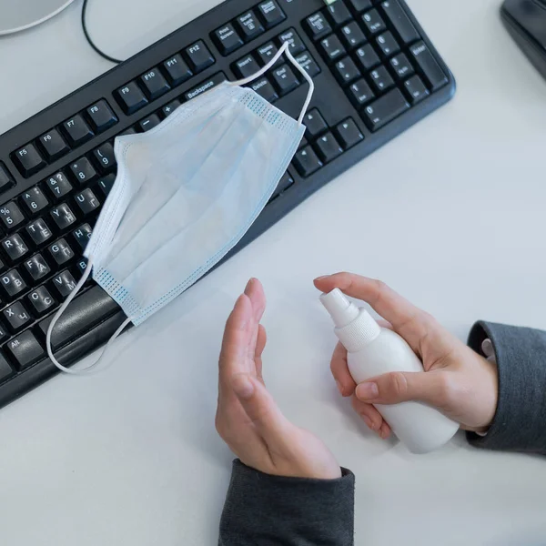 Primo piano del responsabile ufficio mani femminili alla scrivania utilizzando un antisettico per disinfettare. Una donna in giacca e cravatta tratta le mani con un disinfettante che lavora al computer. Maschera sulla tastiera . — Foto Stock