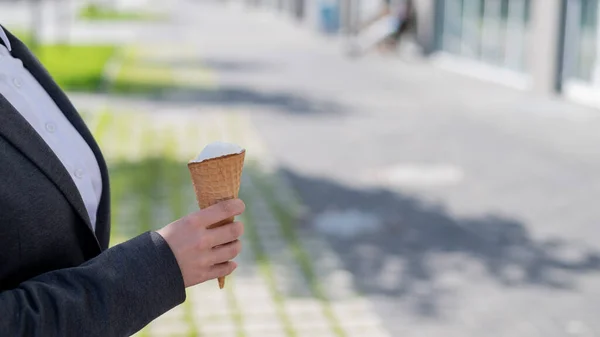 顔のないビジネスマンの女性は屋外を歩き、晴れた夏の日にバニラアイスを食べます。アイスクリームコーンと女性の手のクローズアップ. — ストック写真