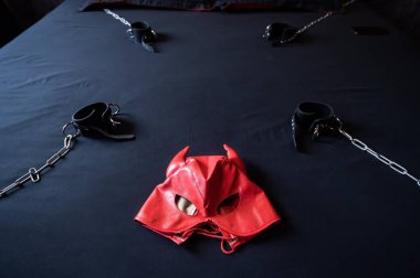 BDSM ekipmanları. Kırmızı deri bir şeytan maskesi ve gri bir çarşafta zincirli siyah kelepçeler. Seks oyuncakları. Hakimiyet. Kimse yok..