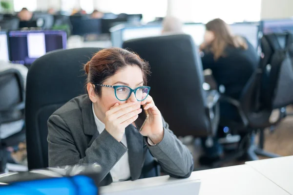 Una mujer se sienta en una oficina en su escritorio y chismorrea por teléfono. Ética corporativa. La empleada de traje cuenta secretos en un smartphone en el trabajo . — Foto de Stock