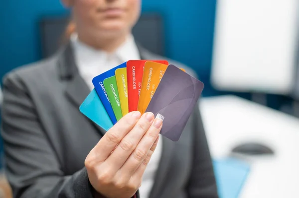 Unrecognizable woman dressed in a suit holds multi-colored plastic credit cards. A faceless bank employee offers a loan. Shopping concept. Close-up of female hands with debit cards.