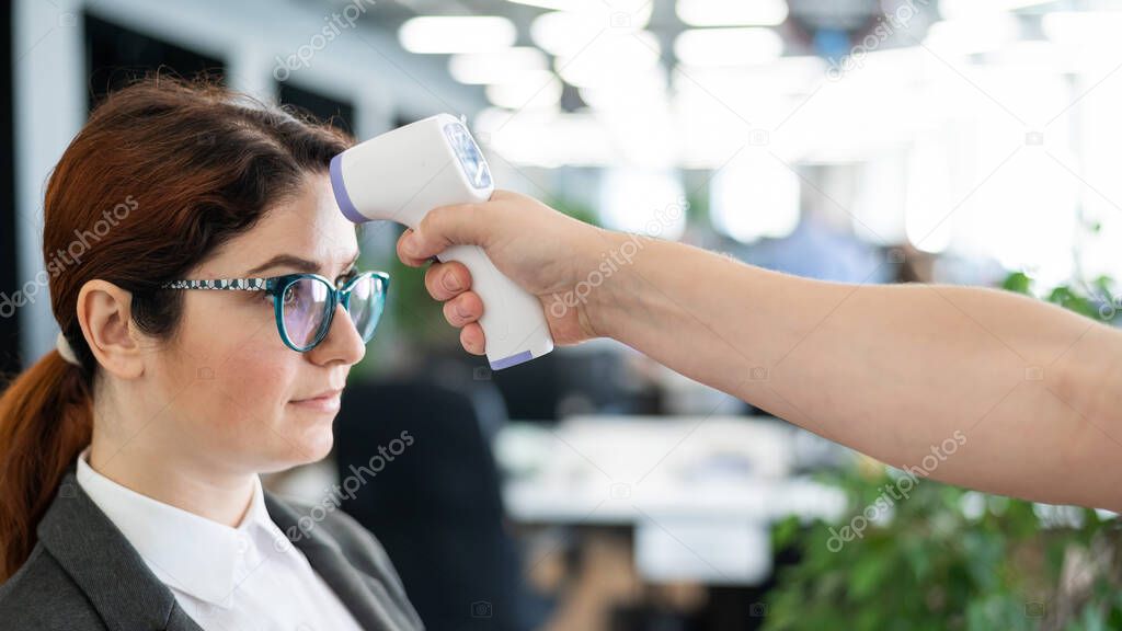 Temperature measurement by electronic infrared thermometer for office staff. Sick woman in a suit. Checking the operation of the gun-thermometer is non-contact. Prevention of the spread of covid-19.