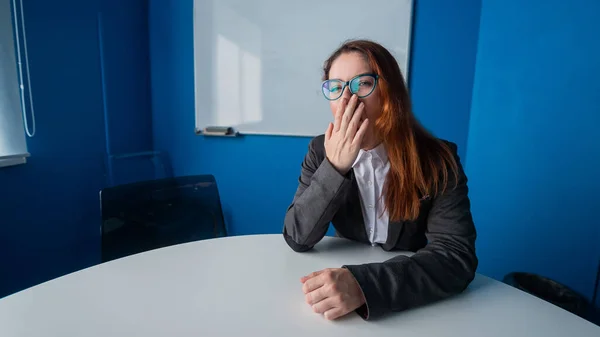 Une femme en costume et lunettes fait bâiller dans la salle de conférence. Une femme gestionnaire de bureau souffrant de fatigue chronique s'assoit à une table dans un atelier ennuyeux. Les partenaires sont en retard pour une réunion d'affaires . — Photo