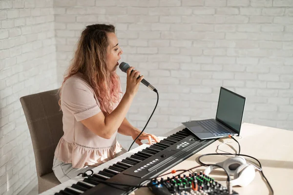 Een vrouw neemt een zangles op met een laptop en begeleidt thuis op een toetsenbord. De leraar zingt een liedje in de microfoon en speelt elektronische piano. Een blogger neemt een video op. — Stockfoto