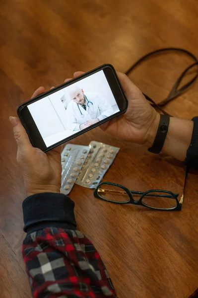 Інтернет-ліки. Стара жінка з коронавірусними симптомами розмовляє на смартфоні з вірусологом. Чоловік слухає скарги на здоров'я літньої жінки на відеозв'язку . — стокове фото