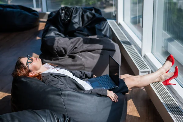 La dama de negocios duerme sentada en una moderna oficina cómoda bolsa de silla bob. Una mujer con traje se quedó dormida en el trabajo en un portátil. El cuidado de la comodidad y la comodidad de los empleados . —  Fotos de Stock