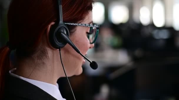 Zadní pohled na ženskou asistentku. Manažer kanceláře se sluchátky odpovídá na telefonáty zákazníků. Neznámá žena v brýlích pracuje jako sekretářka. Centrum volání zaměstnanců. — Stock video