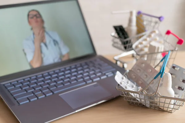 Concepto de medicina y farmacia en línea. Una doctora realiza una consulta en línea y recomienda medicamentos. Mini carro con tabletas en el portátil . — Foto de Stock