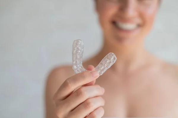 Close-up de dentes transparentes de silicone ortodôntico aligner em mãos femininas. Mulher irreconhecível desfocada segura um retentor de noite removível. Suporte para clareamento dos dentes para um sorriso perfeito . — Fotografia de Stock