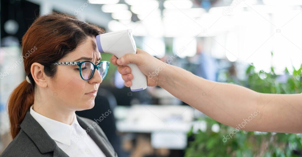 Temperature measurement by electronic infrared thermometer for office staff. Unhappy woman with a fever. A mandatory check at work with a thermometer gun is a non-contact forehead reading. Coronavirus