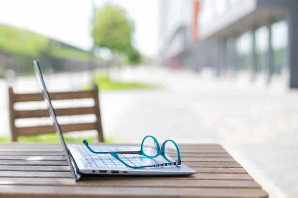 Close-up of glasses and laptop on a wooden table of a summer cafe. Freelancer workplace. Remote workplace. No people. — Stock Photo, Image